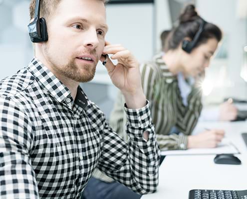 vCIO Portrait of young man wearing headset working with group of help desk operators sitting in row and talking to client